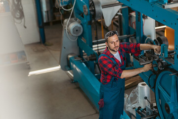 The young craftsman works on a large printing machine in the company.