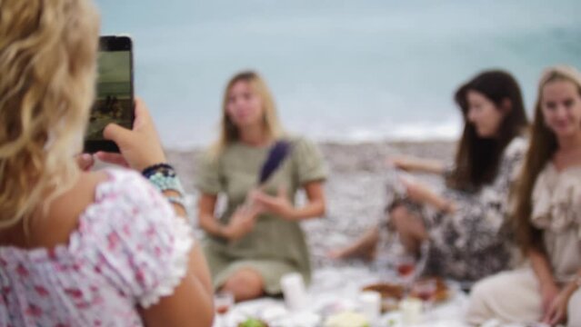 A woman takes pictures on the phone of her friends on the beach by the sea