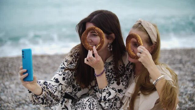 Two women taking pictures on the phone with them holding bagels