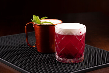 copper mug of moscow mule drink and berry drink with mint leaves seen from the front on the bar...