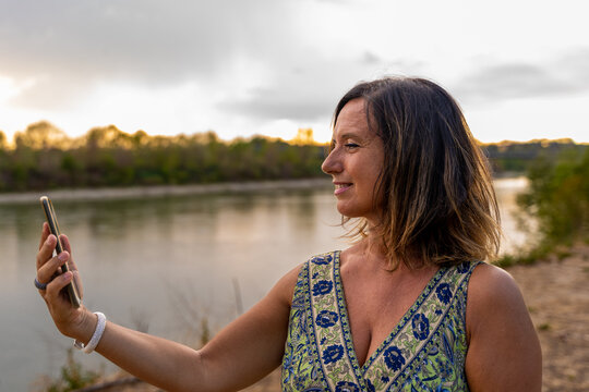 picture of beautiful middle aged lady taking a selfie with smart phone on the banks of the river
