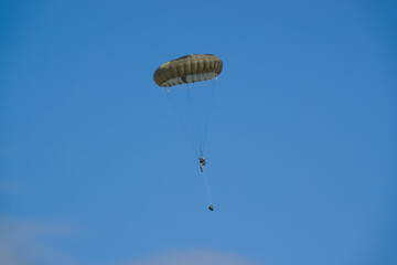 British army paratrooper parachuting on an overhead assault , wearing body armour and webbing with weapons and daysacks suspended by rope below, blue sky