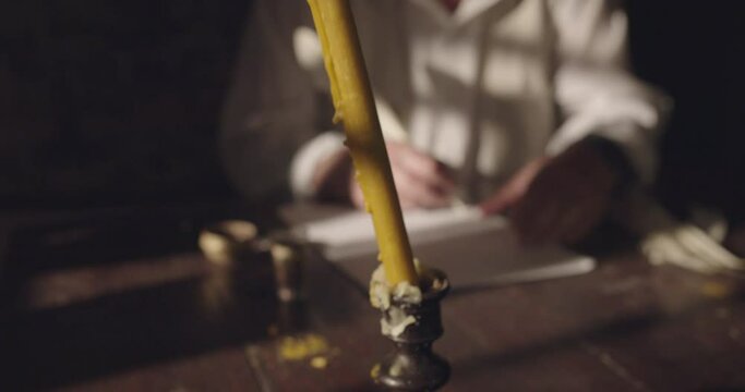 Man writes text on papyrus by the candlelight in the night time, action scene of a medieval writer, crane shot, close up.