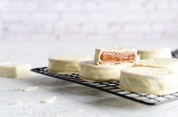 White chocolate alfajores on a dark rack with a piece of white chocolate, on light background. 