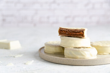 White chocolate alfajores on a beige plate, and a piece of white chocolate, on light background. 