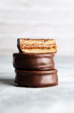 Three dark chocolate alfajores stacked on grey background. 