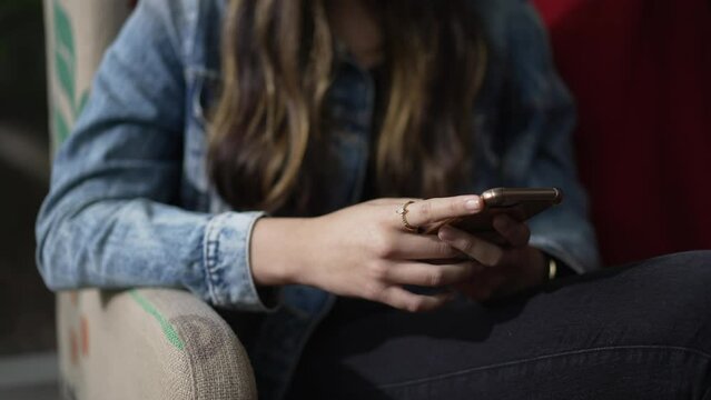 Young woman closeup hands using phone seated at sofa. Close up person typing message with smartphone