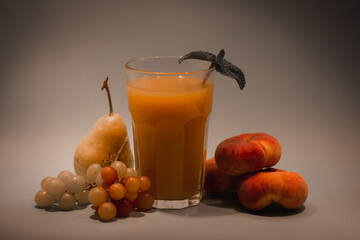 Composition of fruit juice smoothie with mint leaf in faceted glass on table among juicy fresh seasonal fruits - peaches, grapes, pear. Still life fruits faded nostalgic colors. Healthy eat and drink.
