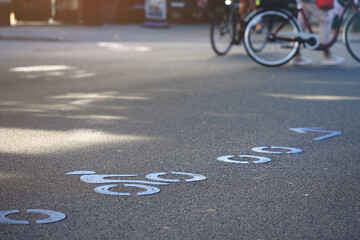 rounded bicycle route symbols painted in blue color on asphalt at an inner city junction. selective focus on single symbol with blurred bikes in background. warm summer evening light © R_boe