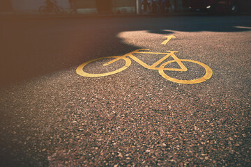 orange bicycle symbol with direction arrow on granular asphalt in swiss city. urban mobility concept. selective focus on wheels of symbol. bus and people blurred in background. striking warm sunlight © R_boe