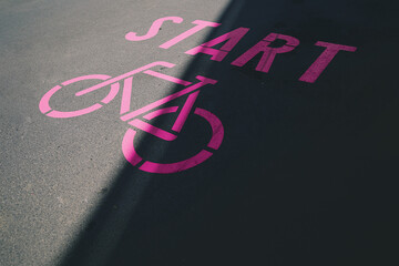 pink bicycle symbol with lettering start painted on inner city asphalt surface. urban mobility and woman sport motivation concept. slogan for ecological traffic turn. selective focus.