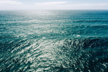 Naklejka na ściany i meble Aerial view over azure ocean with rolling waves. Top view to the ocean in summer sunny day - closeup. Drone view of a Scenic ocean waves. Beautiful Sea blue water with blue sky..