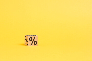 percent sign on wooden cube with copy space. concept of sale and discount, yellow background