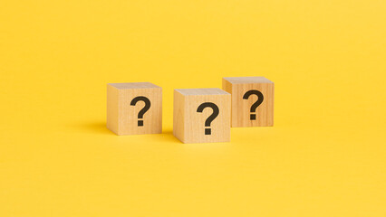 front view on wood cubes with black question marks. many question arising concept, yellow background