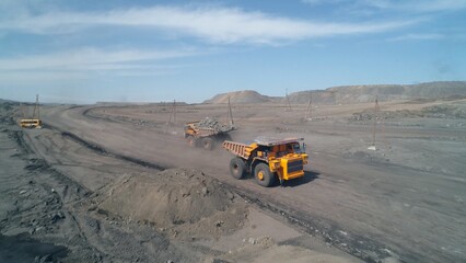 Wide dirt road with huge mining trucks moving towards each other on it