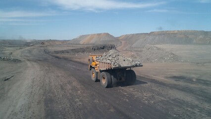 Fototapeta premium Wide dirt road with huge mining trucks moving towards each other on it
