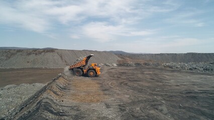 Electric dump truck with raised body unloads stones from stripped coal seam in quarry