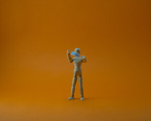 Wooden mannequin with protective surgical mask in orange backgound