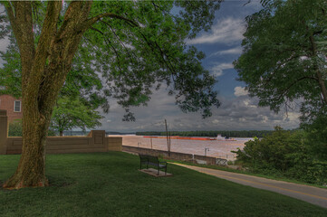 Obraz premium Watching a Barge go up the Mississippi A tow boat with a full load of barges makes it way up river. A serene setting up on top of a bluff with a commanding view of the Mississippi River. 