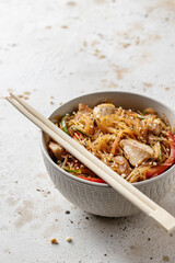Funchose asian salad with chicken and vegetables in bowl with wooden chopsticks on textured brown background with copy space. Food menu