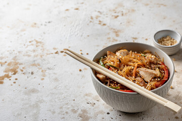 Funchose asian salad with chicken and vegetables in bowl on textured background with text space. Food menu