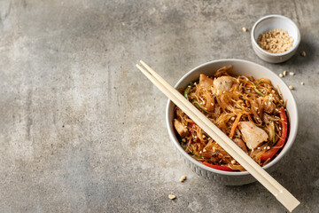 Funchose salad with chicken and vegetables in bowl with wooden chopsticks on green background with copy space. Asian food