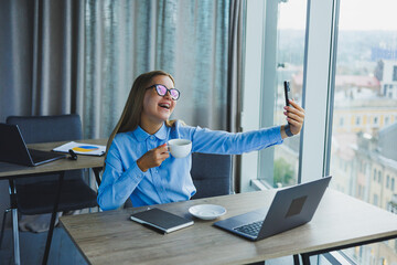 Smart female employee with netbook looking at camera during mobile call, successful freelancer in jacket talking on phone via app