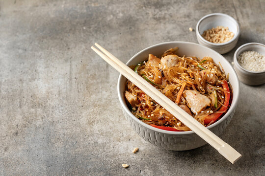 Asian funchose salad with chicken and vegetables in bowl with chopsticks and gravy with ingredients on textured green background with text space. Food menu