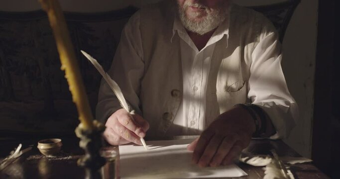 Senior man writing text with a feather on papyrus in the night time, action scene of middle ages time, crane shot, tilt up.