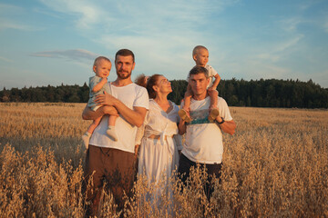two fathers with two children and grandmather walk at sunset in an oat field.