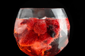 Tall glass of gin & tonic filled with ice and forest fruit. Shot in a studio.