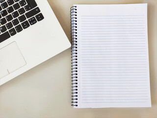 Image showing white office desk and notebook with writing space on the main plane and part of a laptop diagonally