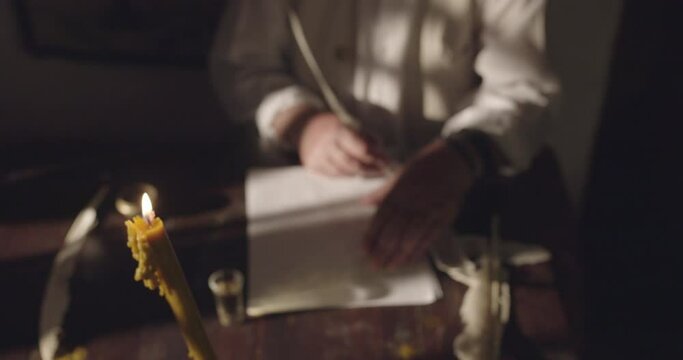Man writes a letter with feather by candlelight, action retro scene, crane, slow-motion shot.