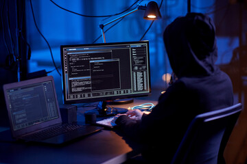 cybercrime, hacking and technology concept - hacker in dark room writing code or using computer...
