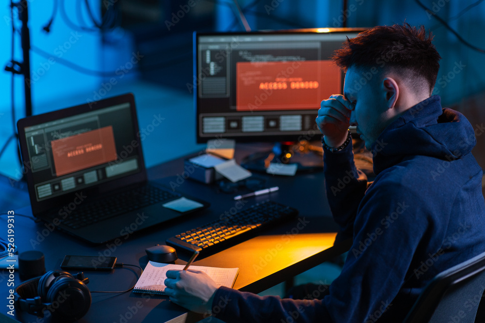 Poster cybercrime, hacking and technology concept - male hacker in dark room writing to notebook and using 