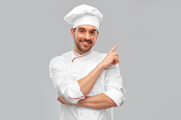 cooking, culinary and people concept - happy smiling male chef in toque pointing to something over...