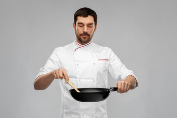 food cooking, culinary and people concept - male chef in jacket with frying pan and spoon over grey background