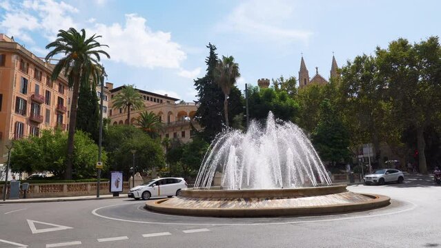 Pan shot of the Fountain at Placa De La Reina (Reina Square) with the cathedral spires in the background - Palma de Mallorca, Spain