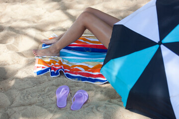 Girl laying on a towel on the beach in the shade under an umbrella.