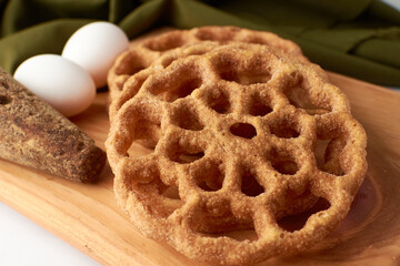 Fritters placed on a wooden base and around a panela and two eggs.