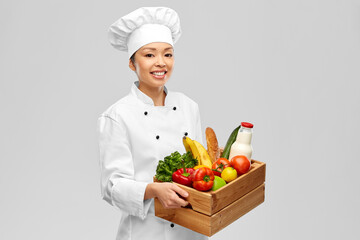 cooking, culinary and people concept - happy smiling female chef in toque holding food in wooden box over grey background
