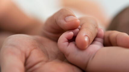 Close up mother holding hands newborn boy in a room with a lot of sunlight. Baby