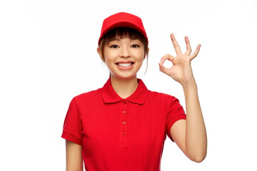 profession, job and people concept - happy smiling delivery woman in red uniform showing ok gesture...