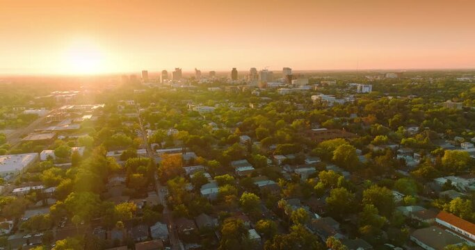 Last rays of setting sun over the beautiful green city. Few multi-storied buildings standing out at the backdrop of orange sky.