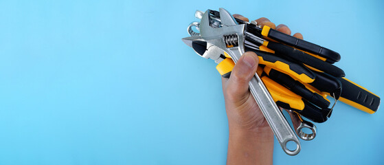 hand holding  different types of black yellow hand tools isolated blue background