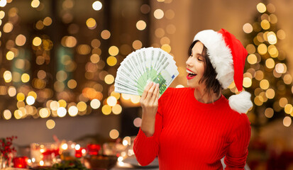 christmas, holidays and finance concept - happy smiling woman in santa helper hat holding euro...