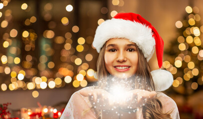 christmas, holidays and magic concept - happy smiling teenage girl in santa helper hat holding...