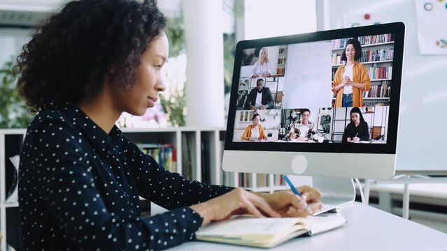 Online education, e-learning. Smart african american curly girl, sits at a desktop in front of a computer screen, concentrated watches and listens to an online lecture, takes notes, gain knowledge