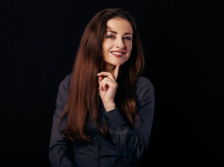 Beautiful thinking toothy smiling business woman with finger under the face in blue shirt on black background with empty copy space for text. Closeup