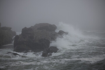 Ocean waves crashing onto a rocky shore on a foggy morning